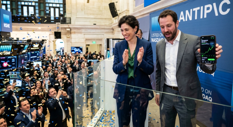 Illustration of an AI company’s stock market debut, with two executives celebrating above a crowded trading floor and a smartphone displaying a rising stock chart.