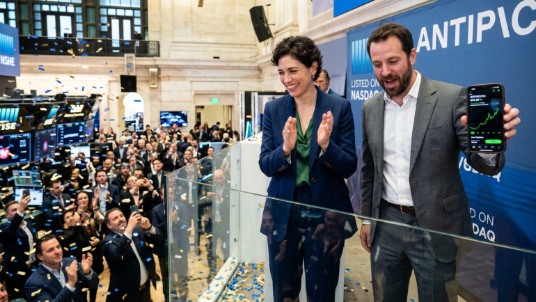 Illustration of an AI company’s stock market debut, with two executives celebrating above a crowded trading floor and a smartphone displaying a rising stock chart.